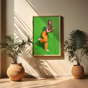 A framed poster featuring a green recycled paper matt-coated with an image of a person wearing orange overalls, displayed in a room with two potted plants. 6912 TrueColor