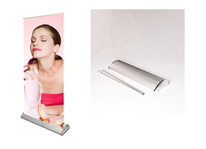 A display of a pull up banner stand with a silver aluminum base, support pole, and a carry bag. The banner shows a woman against a pink background.