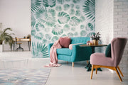 Living room with green wallpaper featuring a leafy pattern, a blue sofa, a pink armchair, and a white round side table with a plant on it.